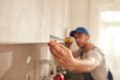 Handyman measuring a kitchen cabinet with a tape measure, focusing on precise alignment during installation.
